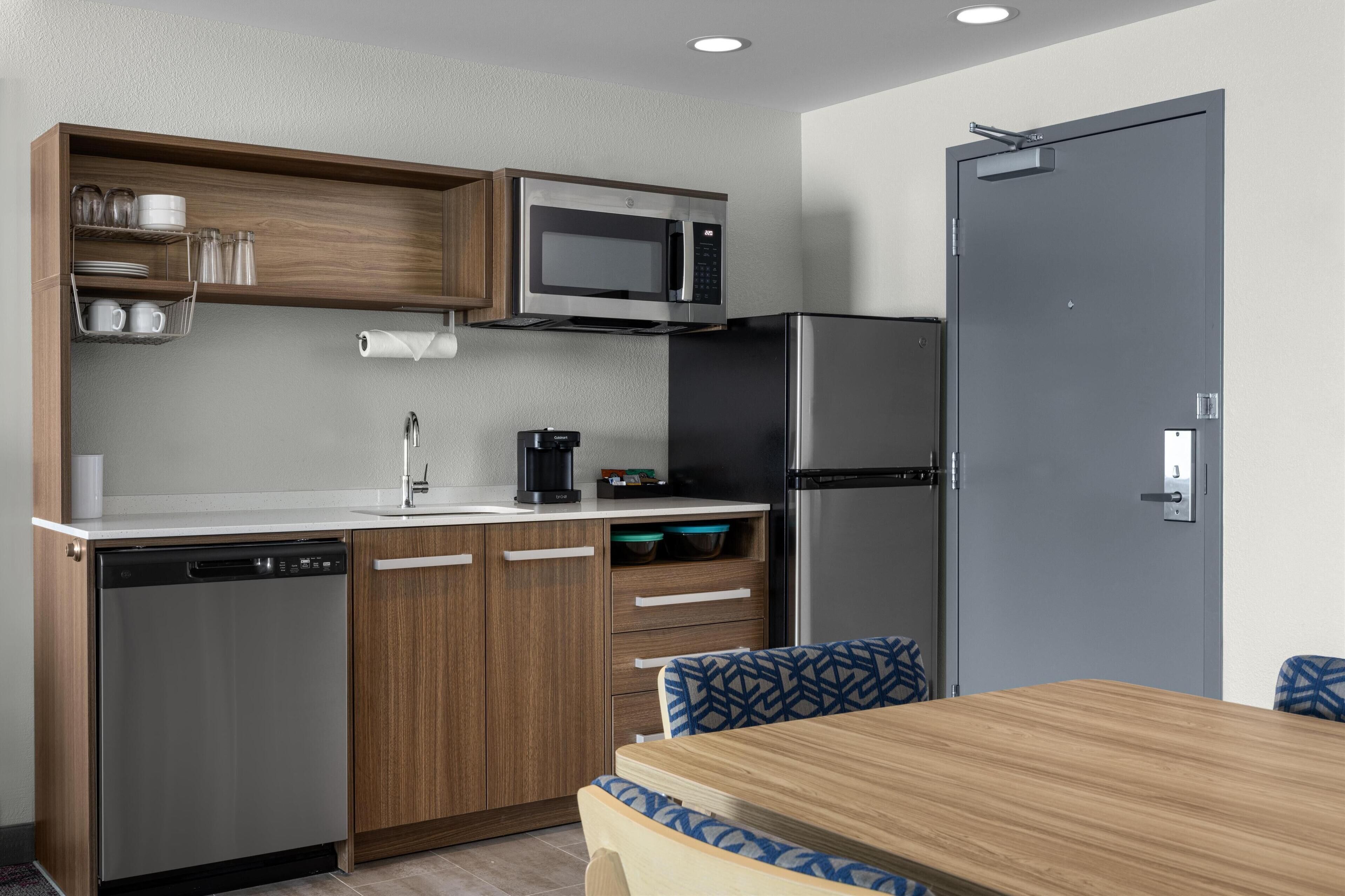 A compact kitchen with a microwave, refrigerator, dishwasher, and wooden cabinets.