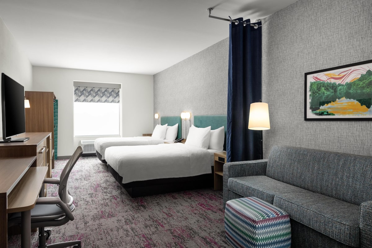 A hotel room with two beds, a desk, a chair, a sofa, and a TV.