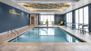 Ein Innenpool mit geometrischem Deckenmuster, eine Sitzgelegenheit am Pool sowie ein Schild mit der Aufschrift 'POOLSIDE IS MY VIBE'.