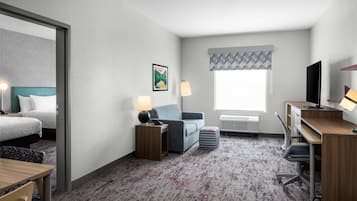 A hotel room with a bed, a desk, a chair, a sofa, a lamp, a TV, and a window with a patterned curtain.