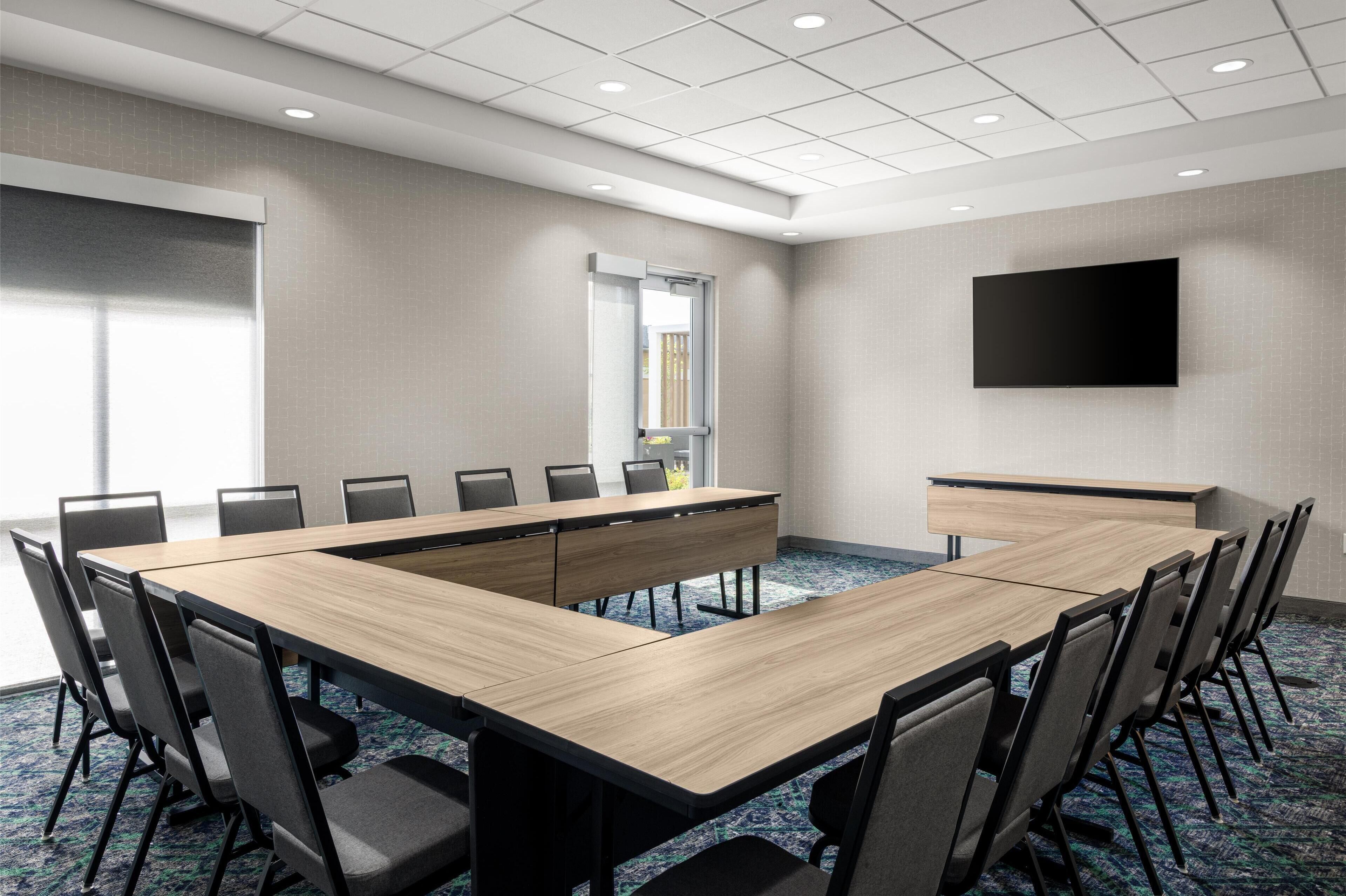 A conference room with a long table, chairs, a TV, and a window.