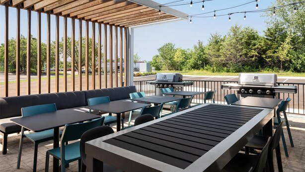 Eine Terrassensitzgelegenheit mit Sitzplätzen, Tischen, Lichterketten und einem Grill.