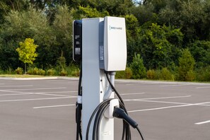 Una estación de carga para vehículos eléctricos con el rótulo 'EVOCHARGE' en un estacionamiento con árboles al fondo.