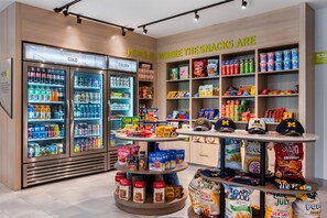 Una sección de aperitivos y bebidas con opciones refrigeradas, barras energéticas y una exhibición de gorras con la marca.