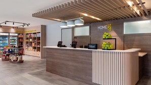 Ein Hotel-Empfangsbereich mit einem Holzbüro, einem Verkaufsautomaten und einem Schild mit der Aufschrift 'HOME 2'.