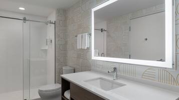 A modern bathroom with a glass shower enclosure, a white sink with a large mirror, and patterned wall tiles.