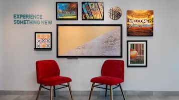 A wall with framed artwork, two red chairs, and a large framed picture.