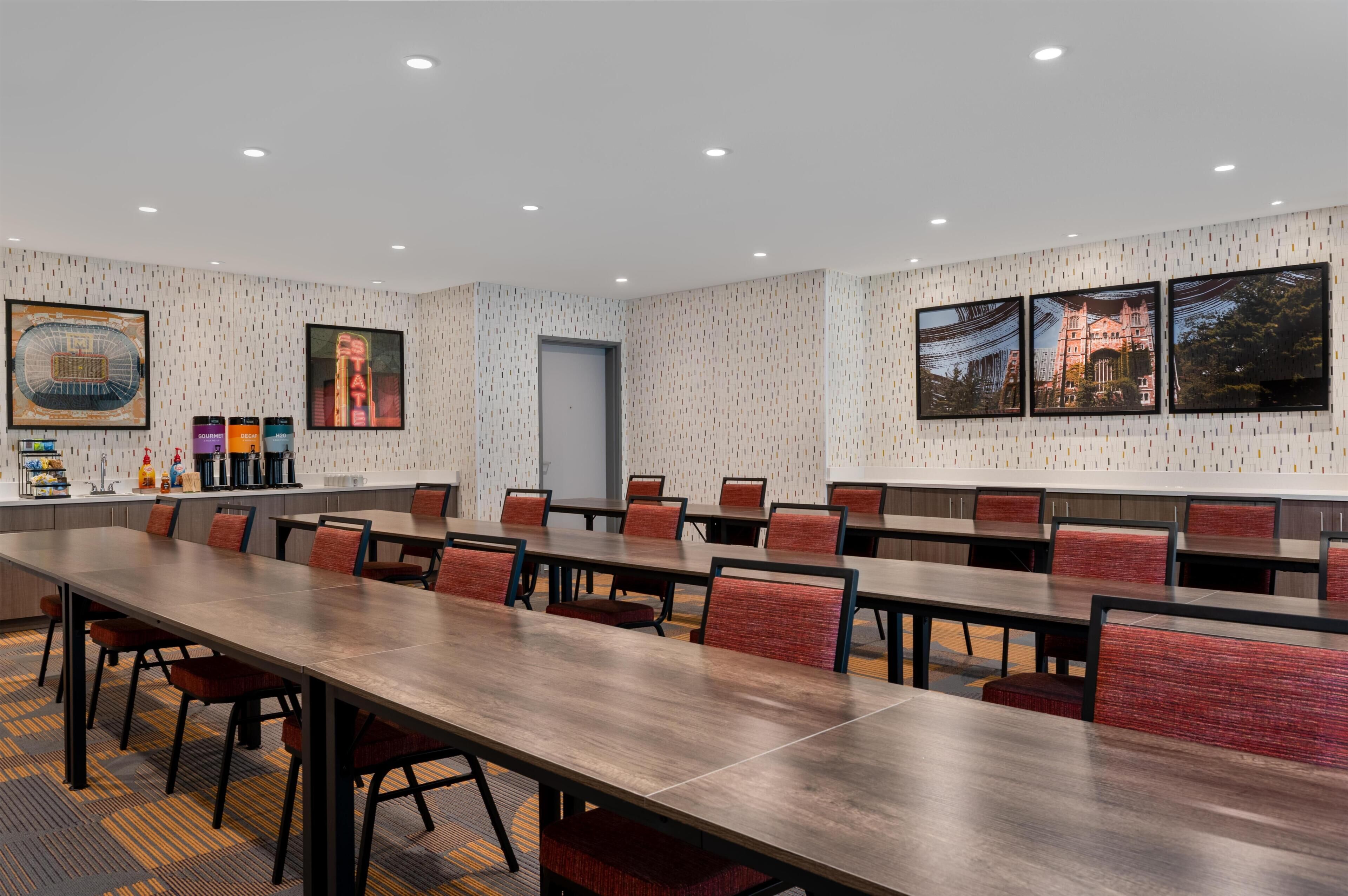 A conference room with long tables and chairs, framed pictures on the walls, and a patterned wallpaper.