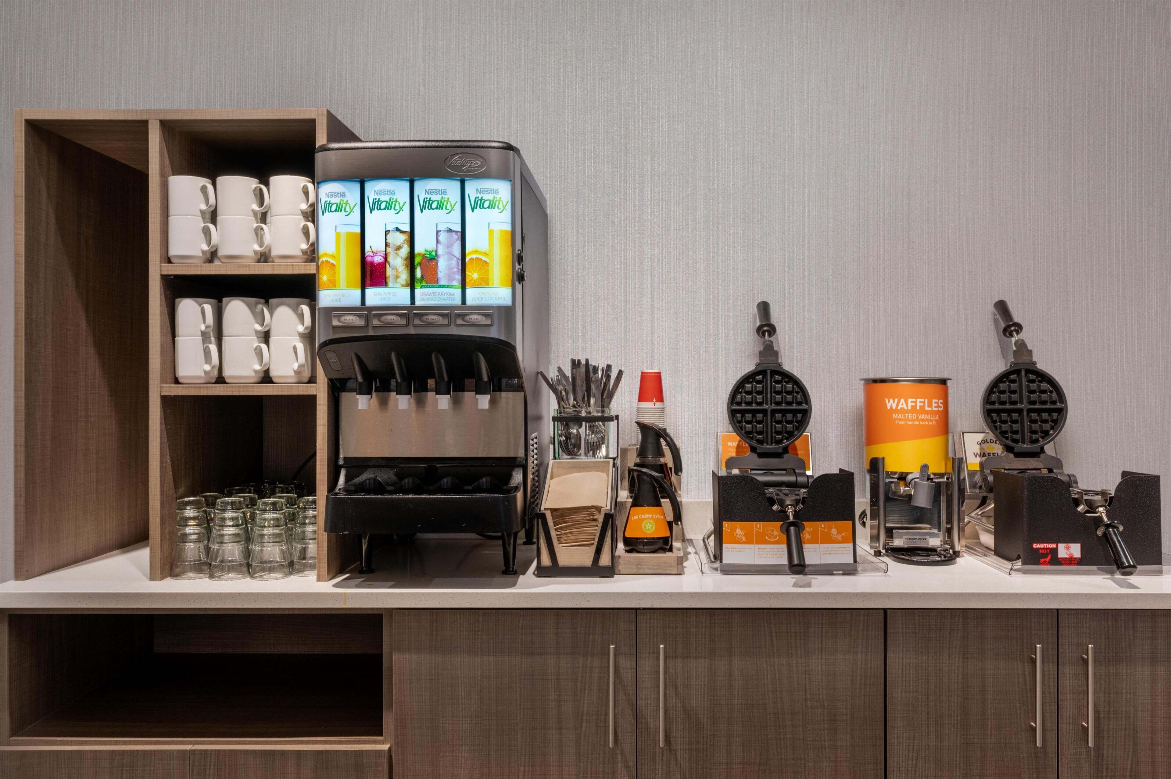 A coffee station with a coffee machine, waffle maker, and waffle container.