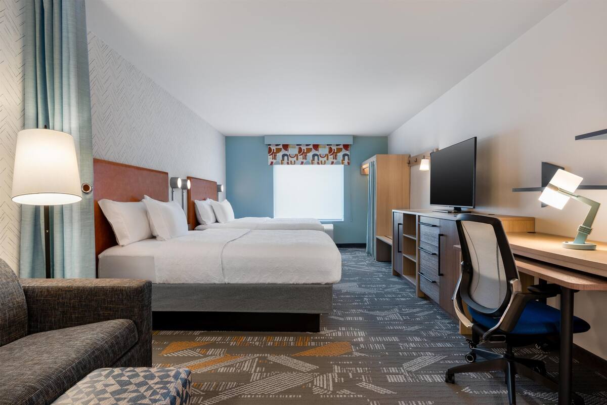 Habitación de hotel con cama, escritorio, silla, televisor y lámpara.