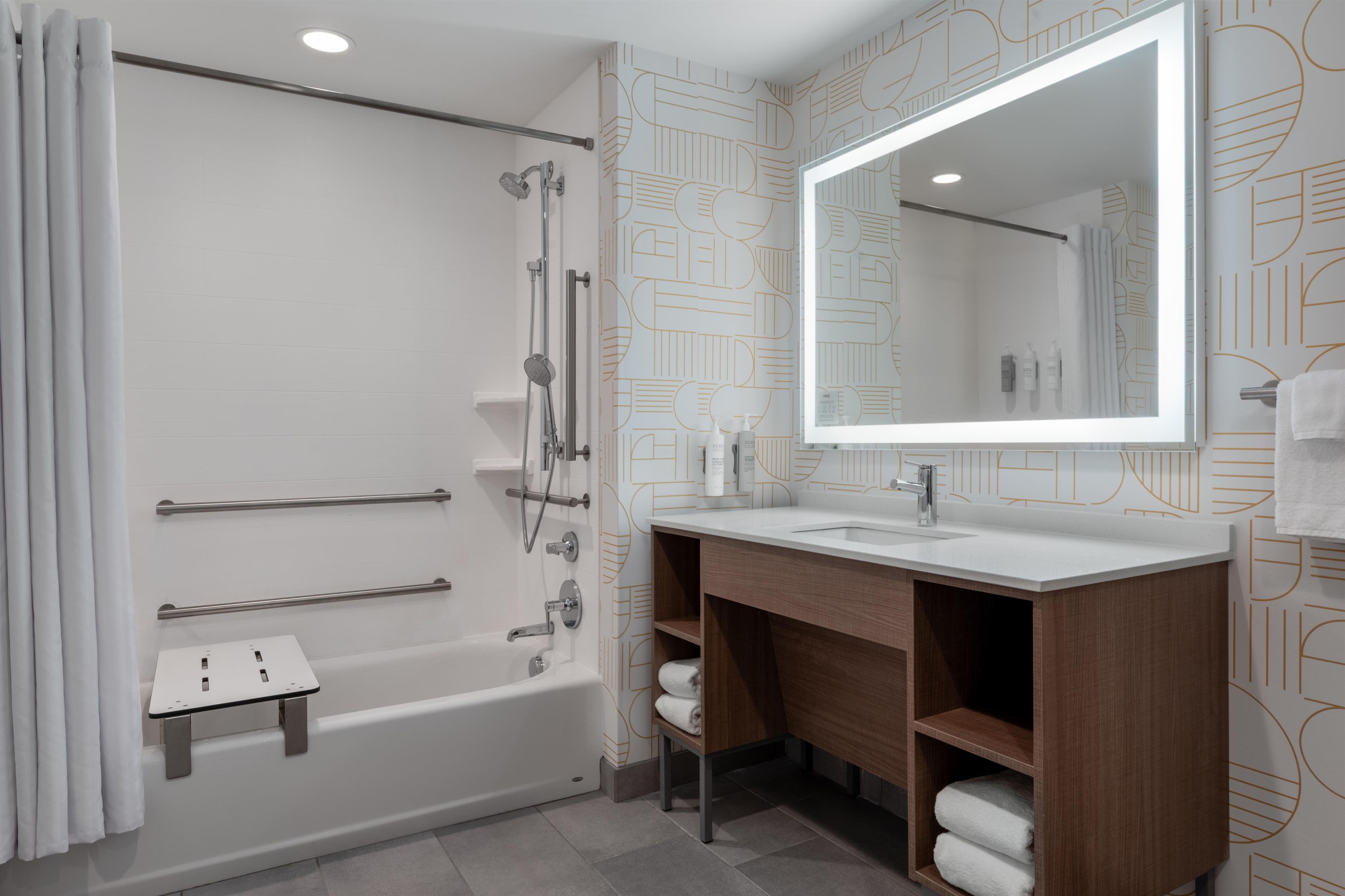 Un baño moderno con bañera, ducha, tocador con espejo y toalleros.