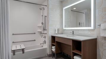 Un baño moderno con bañera, ducha, tocador con espejo y toalleros.