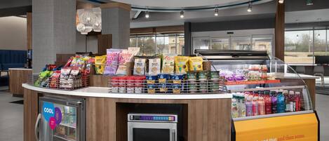 Un bar de aperitivos con diversos productos envaselados, un refrigerador para bebidas y un microondas.