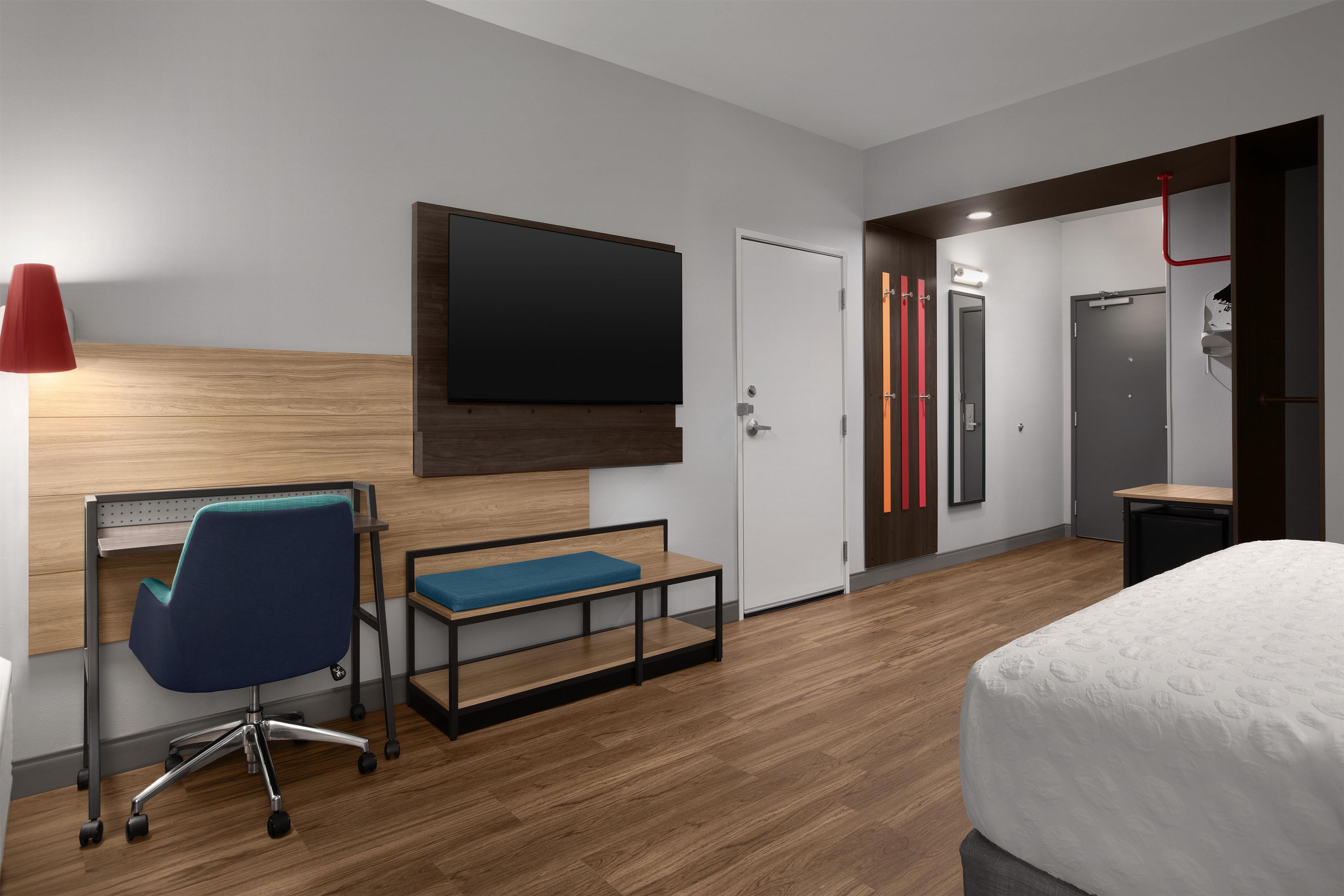 A modern hotel room with a bed, desk, chair, TV, wardrobe, and a bathroom.