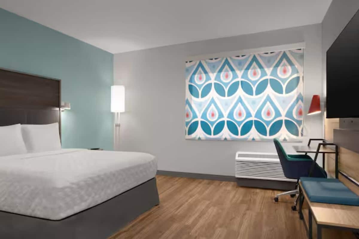 Habitación de hotel con cama, escritorio, silla y ventana con cortinas estampadas.