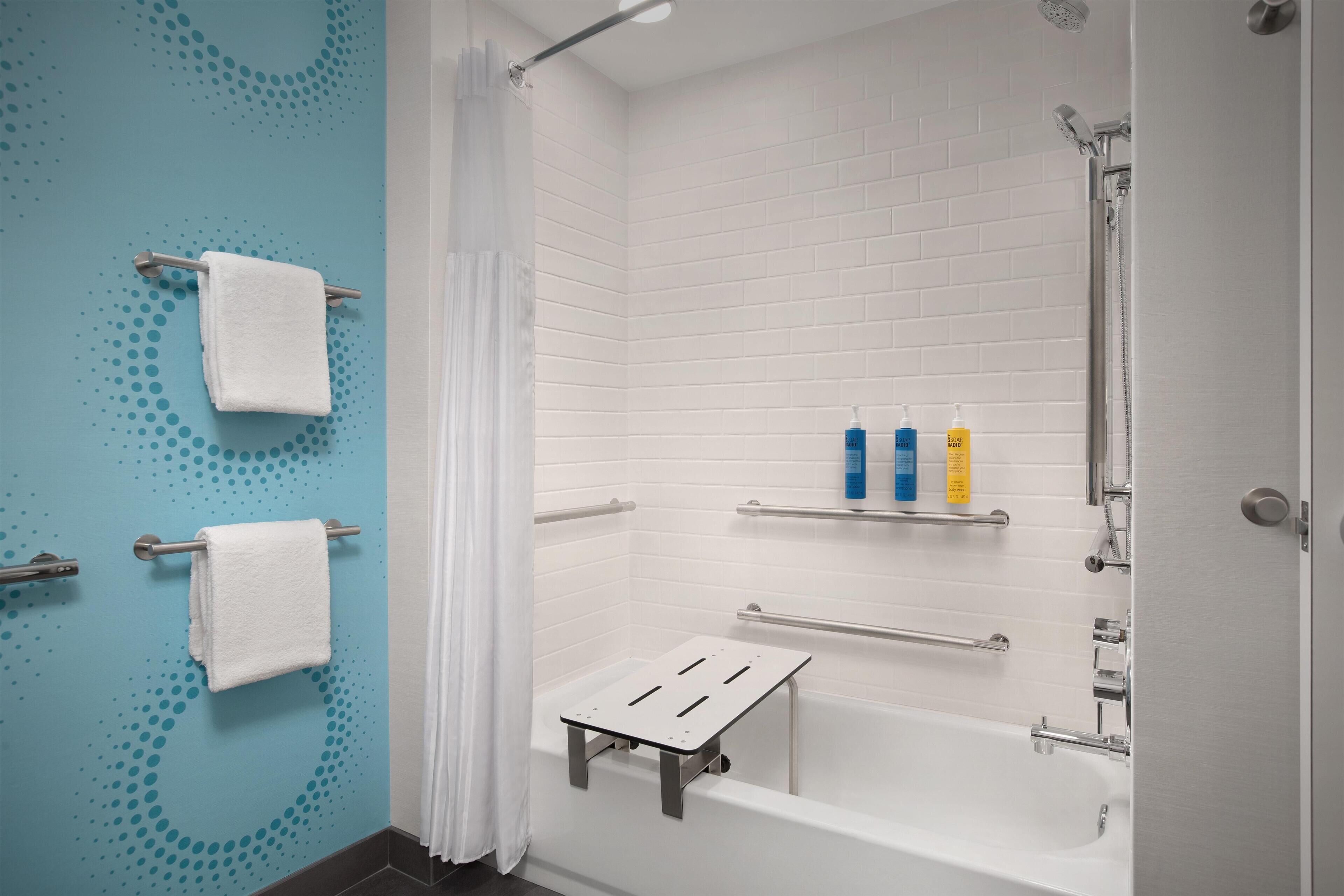 Un baño moderno con una bañera blanca, zona de ducha y pared azul con estampado de lunares. Hay dos toallas colgadas en barras para toallas y un estante con artículos de aseo.