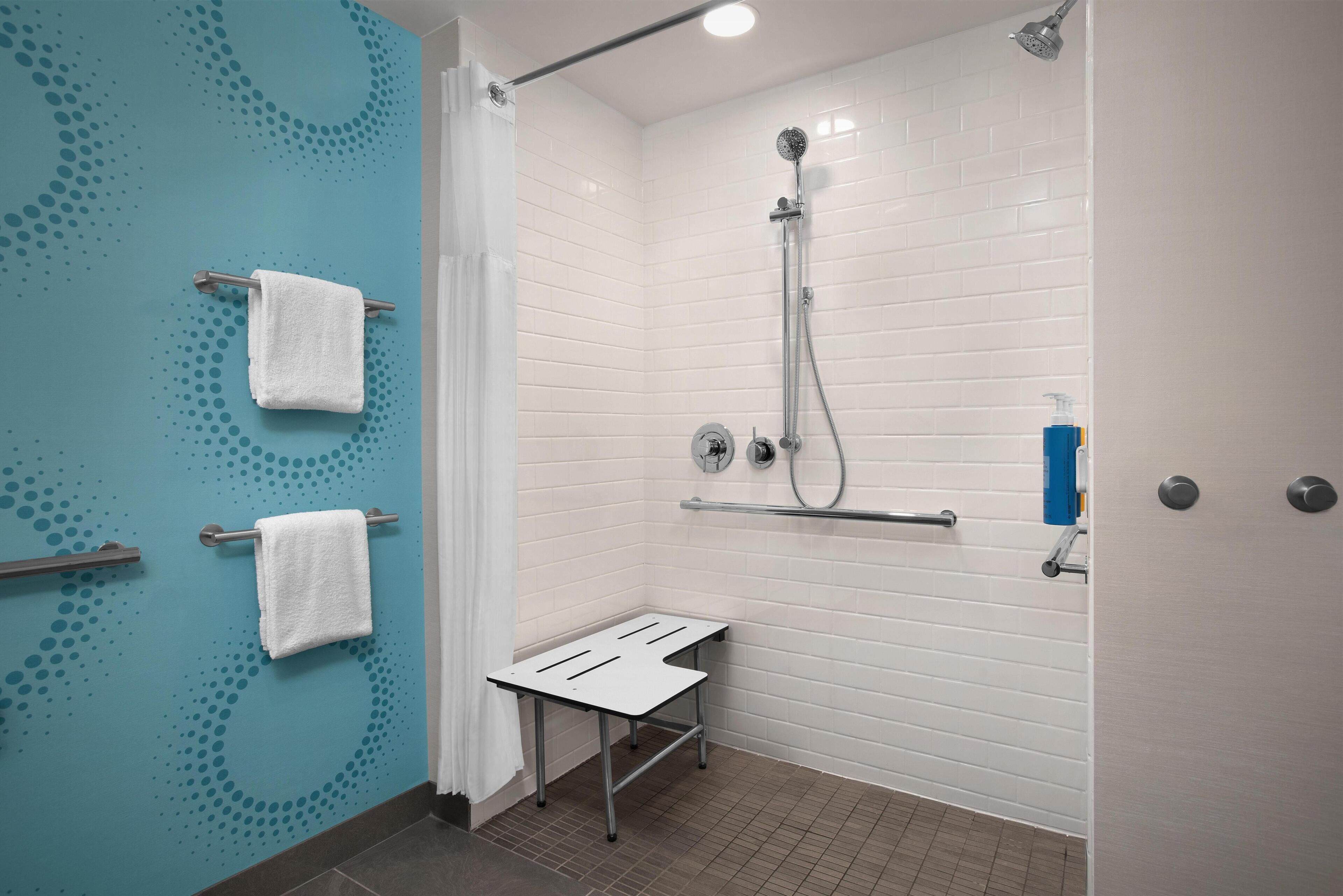 A modern bathroom with white tiled walls, a shower with a handheld showerhead, a towel rack, and a small bench.