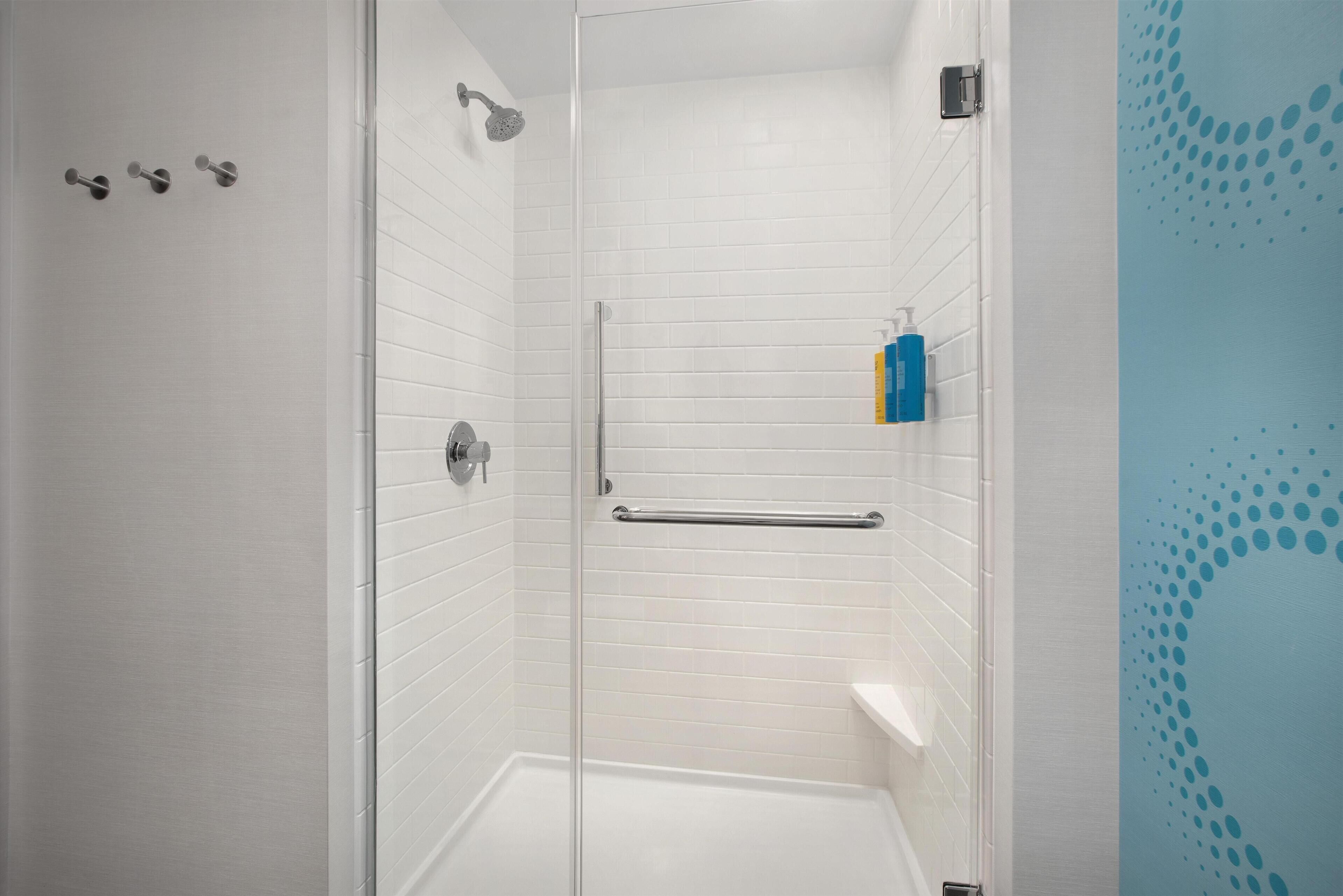 Ducha a ras de suelo con paredes de azulejos blancos, puerta de cristal y barra de apoyo.