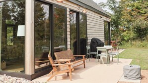 A modern house with large glass doors, outdoor seating, and a barbecue area.