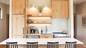 A modern kitchen with wooden cabinets, a large island with bar stools, a coffee maker, and a kettle.