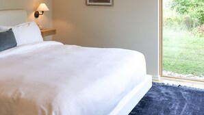 A neatly made bed with white linens, a bedside lamp, and a framed botanical print on the wall.