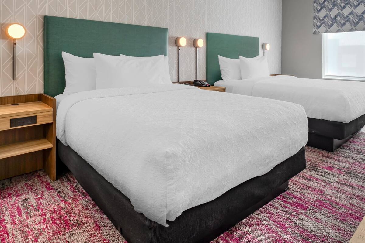 A hotel room with two beds, each with a green headboard, white bedding, and bedside lamps.