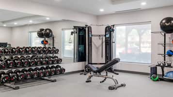 Un gimnasio con equipo de levantamiento de pesas, mancuernas y pelotas de ejercicio.