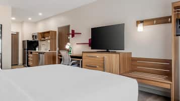 Een moderne hotelkamer met een groot bed, houten meubels, een flatscreen televisie en een kitchenette.