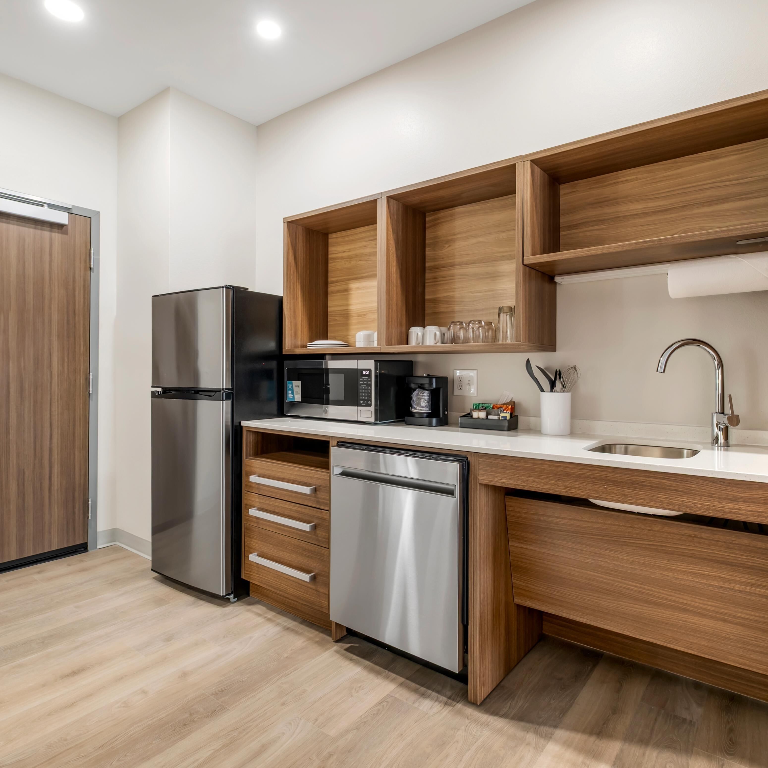 Una cocina moderna con un refrigerador de acero inoxidable, un microondas integrado, una cafetera y un lavavajillas.