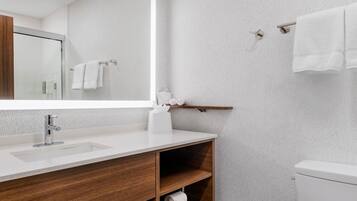 A modern bathroom with a large mirror, white sink, wooden vanity, and a toilet.