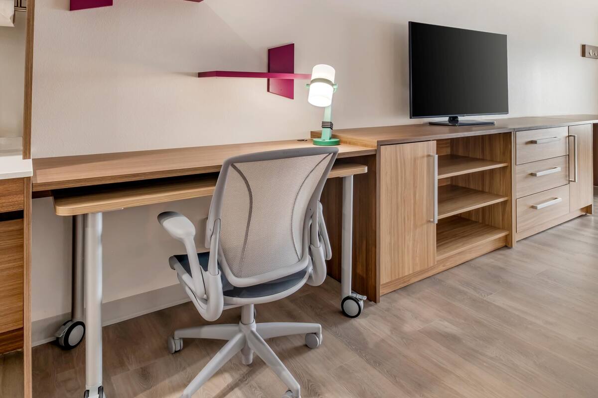 A modern office space with a wooden desk, a computer, a chair, and a TV.