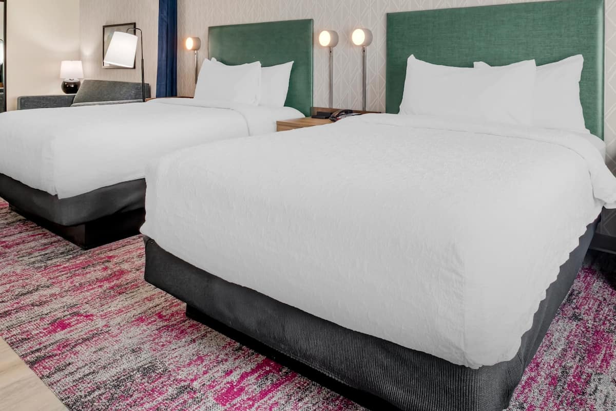 A hotel room with two beds, a desk, a chair, and a nightstand.