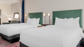A hotel room with two beds, a desk, a chair, and a nightstand.