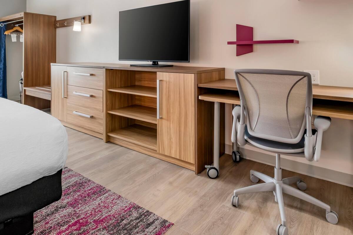 A modern bedroom with a bed, a desk with a computer, a TV, and a chair.