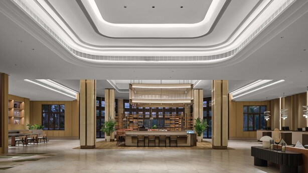 Een ruime lobby met een centraal gelegen receptiebalie, grote ramen en een modern plafondontwerp.