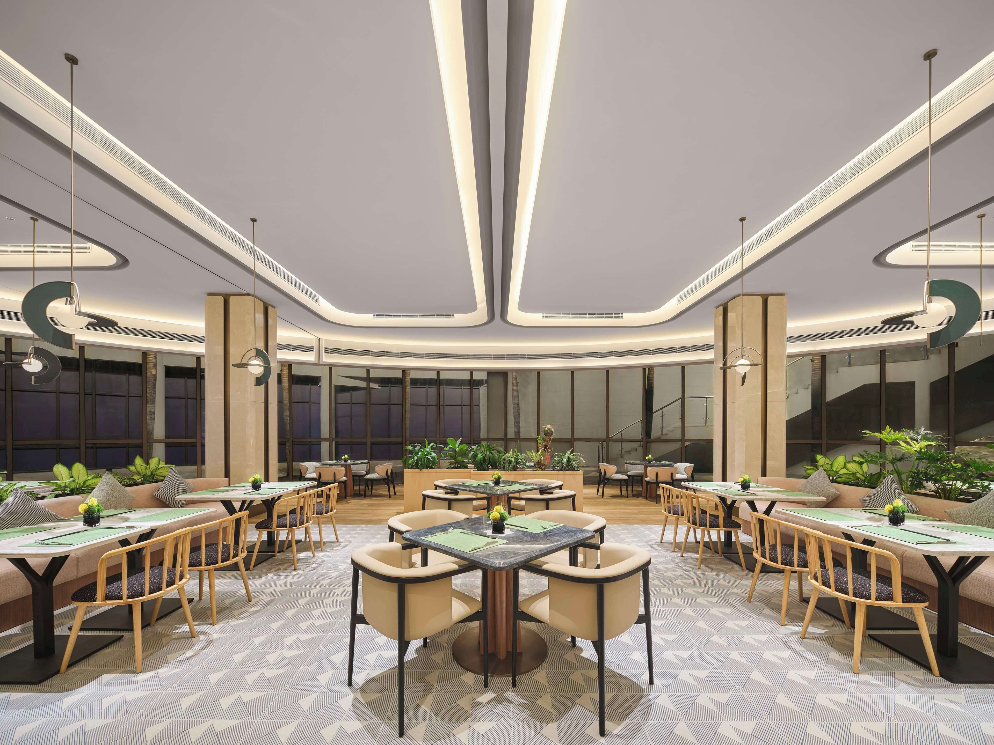 A modern dining area with multiple tables and chairs, large windows, and a central staircase.