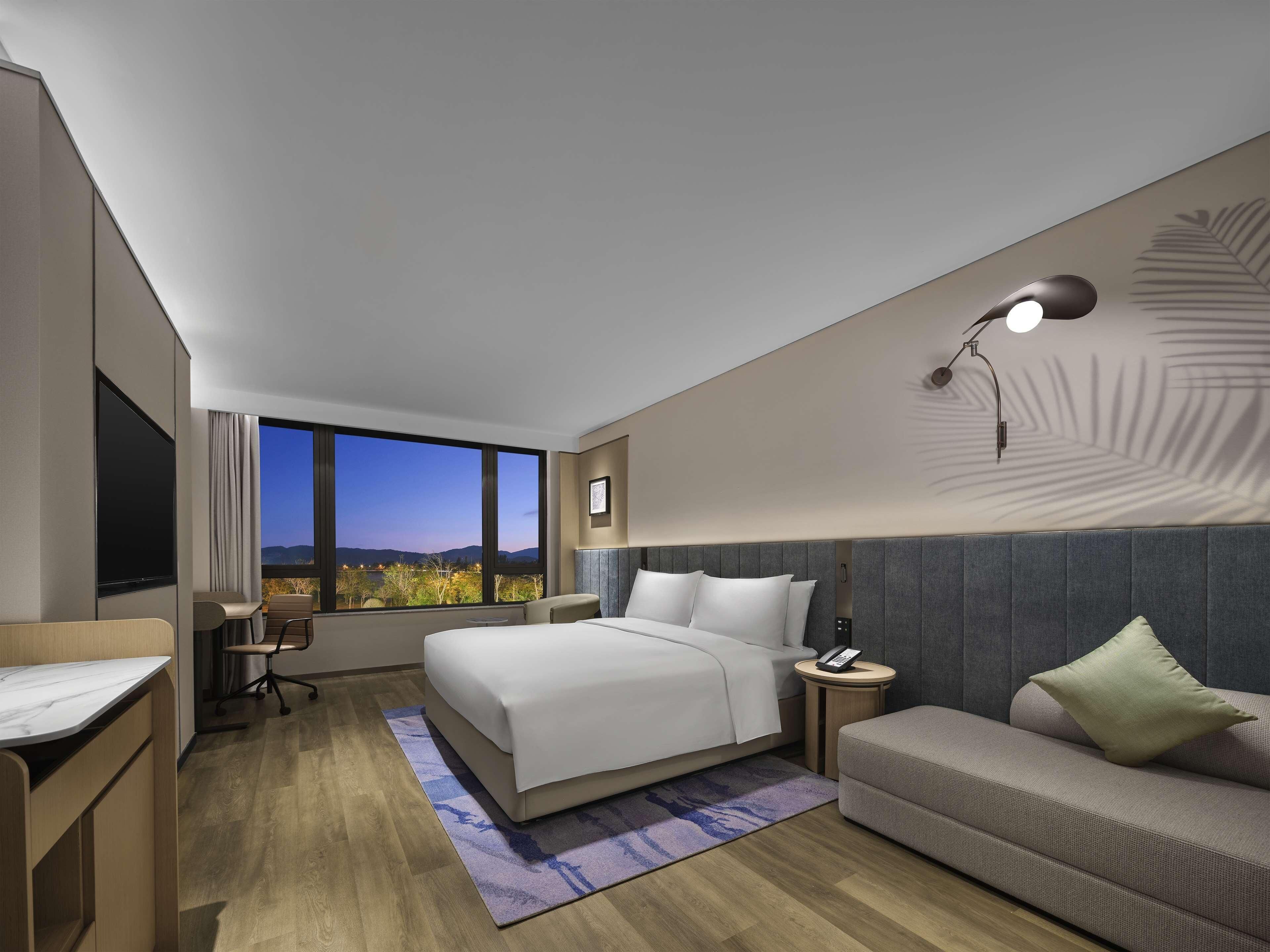 Une chambre d’hôtel moderne dotée d’un grand lit, d’un canapé, d’un bureau et offrant une vue sur les montagnes.