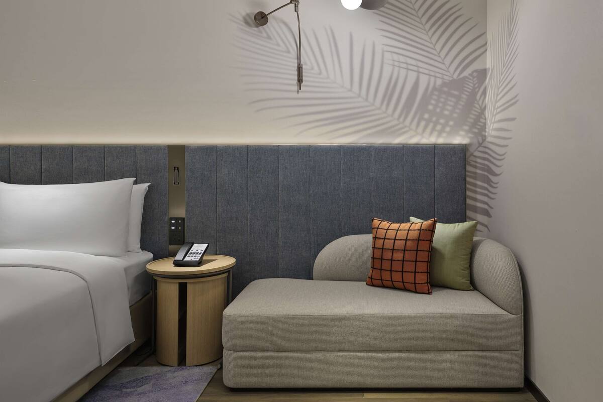 A hotel room with a bed, a sofa, a bedside table with a phone, and a wall-mounted lamp.