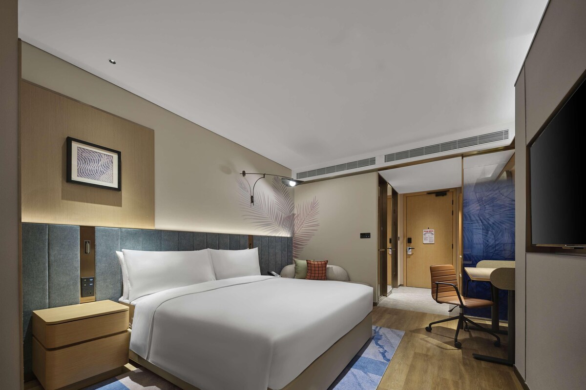 A modern hotel room with a large bed, bedside tables, a desk, and a chair.