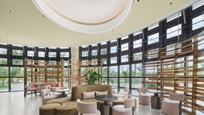 Een ruime lobby met een modern design, met een centraal zithoek met banken en fauteuils, grote ramen met uitzicht op het omliggende landschap, en een hoge plafond met inbouwverlichting.
