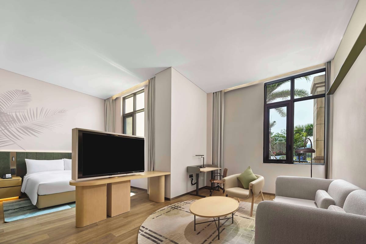 A modern hotel room with a bed, a TV, a sofa, a chair, and a desk.