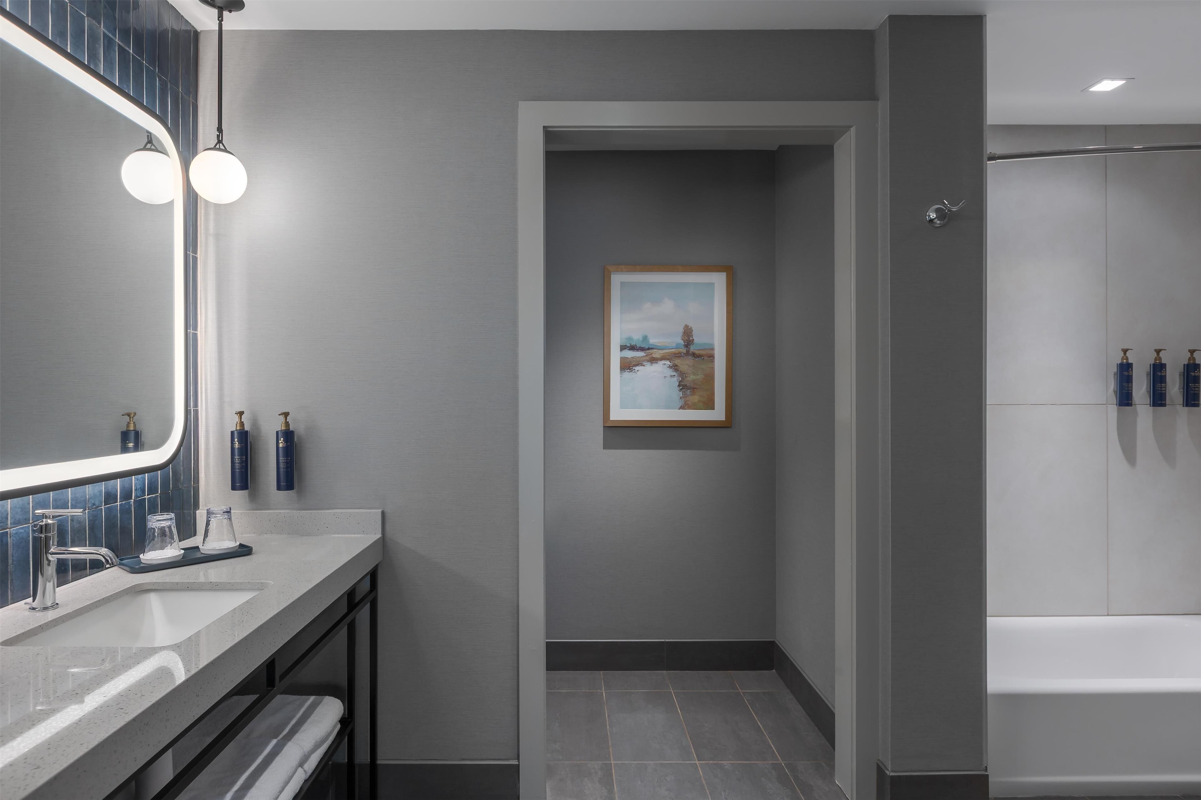 A modern bathroom with a large mirror, a sink, a framed painting, and a shower area.