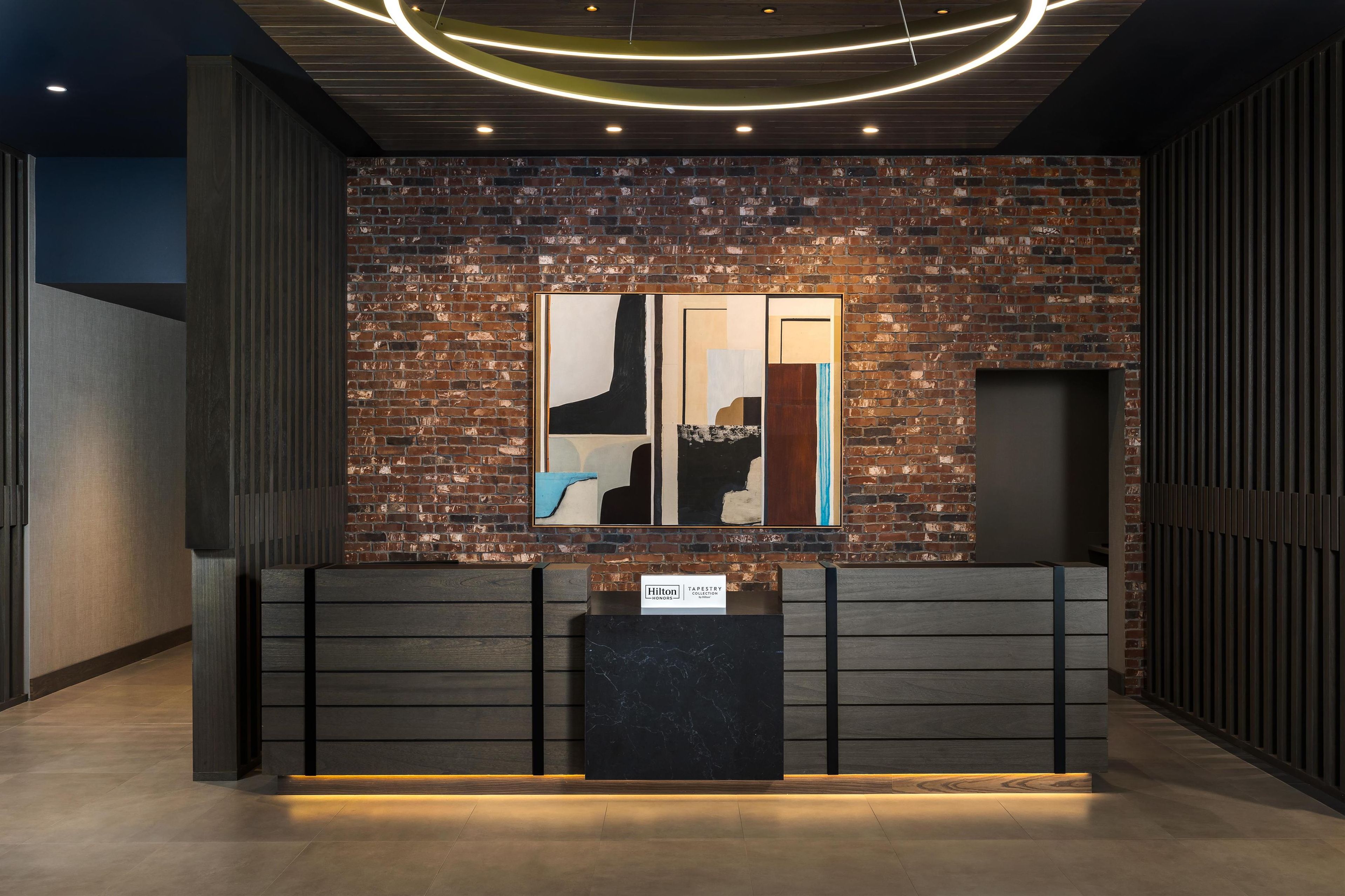 Een receptiebalie met een modern ontwerp, een bakstenen muur en abstracte kunstwerken erboven.