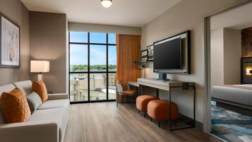 Une chambre d’hôtel moderne équipée d’un canapé, d’un bureau, d’une télévision et offrant une vue sur le paysage urbain.