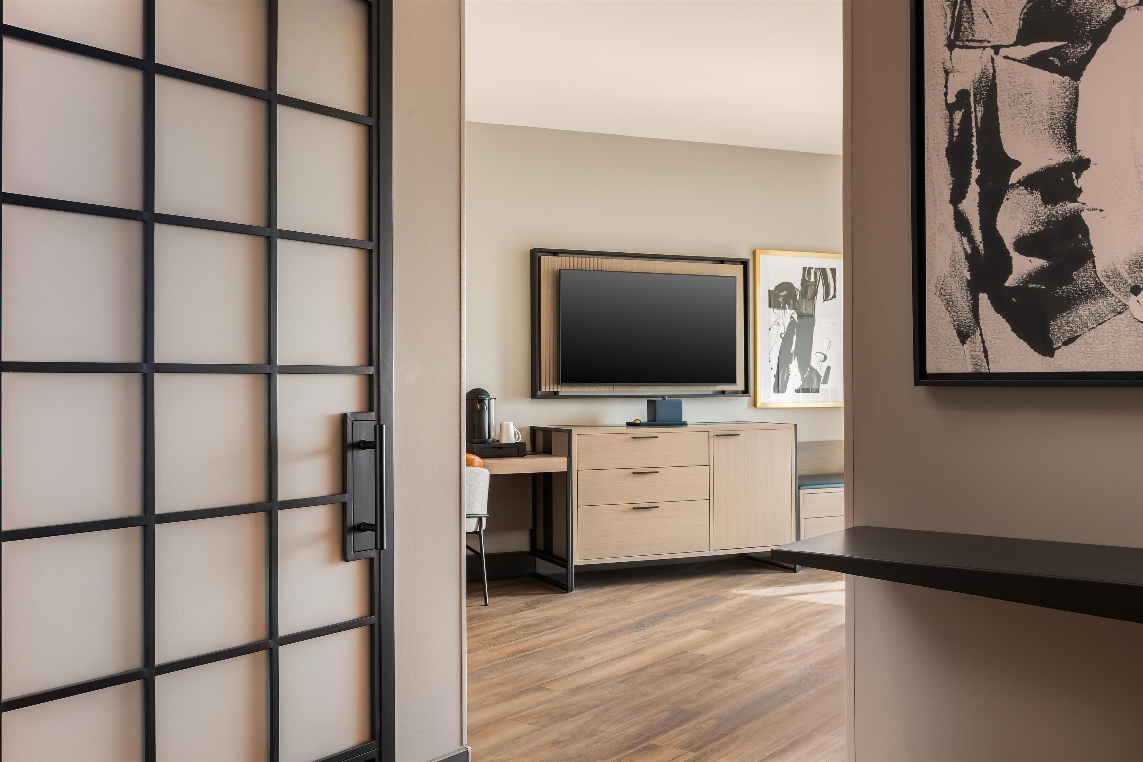 A modern room with a sliding door, a flat-screen TV, a desk, and a cabinet.