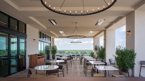 An outdoor dining area with multiple tables and chairs, a large circular chandelier, and potted plants. - Hotel Avail Rogers, Tapestry Collection By Hilton (Rogers)