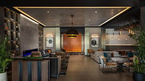 A modern lobby with a reception desk, seating area, and a brick wall with a hanging light fixture. - Hotel Avail Rogers, Tapestry Collection By Hilton (Rogers)