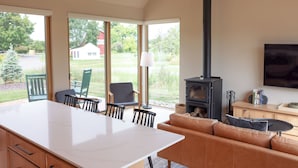 Un vaste espace de vie comprenant une grande table blanche, un canapé en cuir et un poêle à bois noir.
