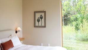 Une chambre à coucher avec un grand lit, une table de chevet, une lampe fixée au mur et un tableau représentant des coquelicots.