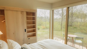 A bedroom with a large window, a wooden wardrobe, and a small table with chairs outside.